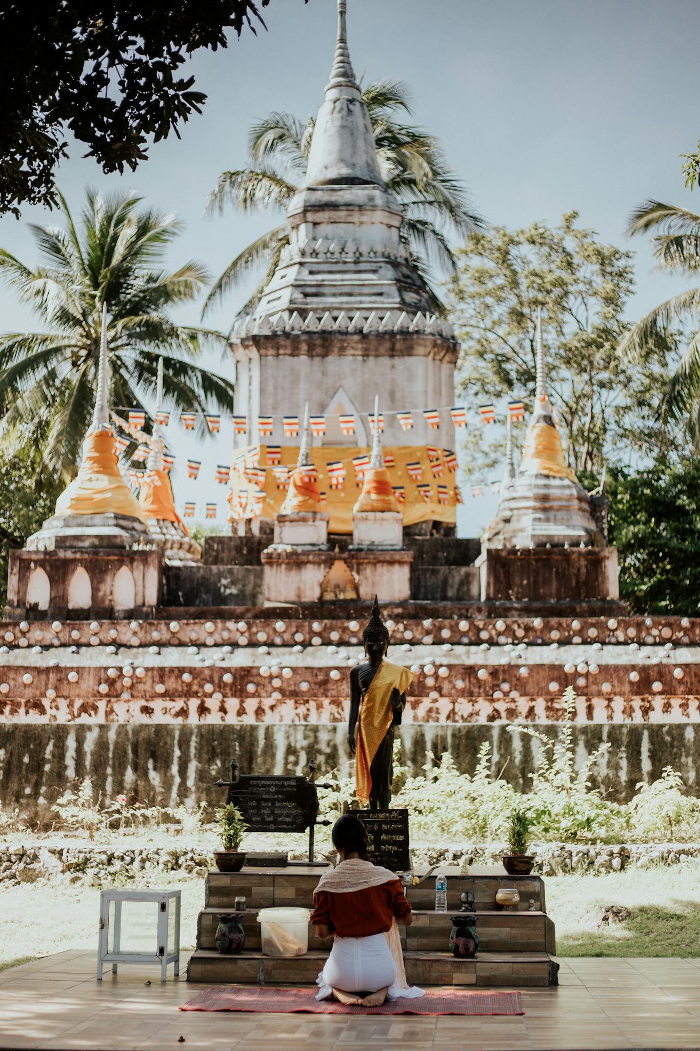 A woman kneels in prayer at a historic Buddhist temple surrounded by nature.
