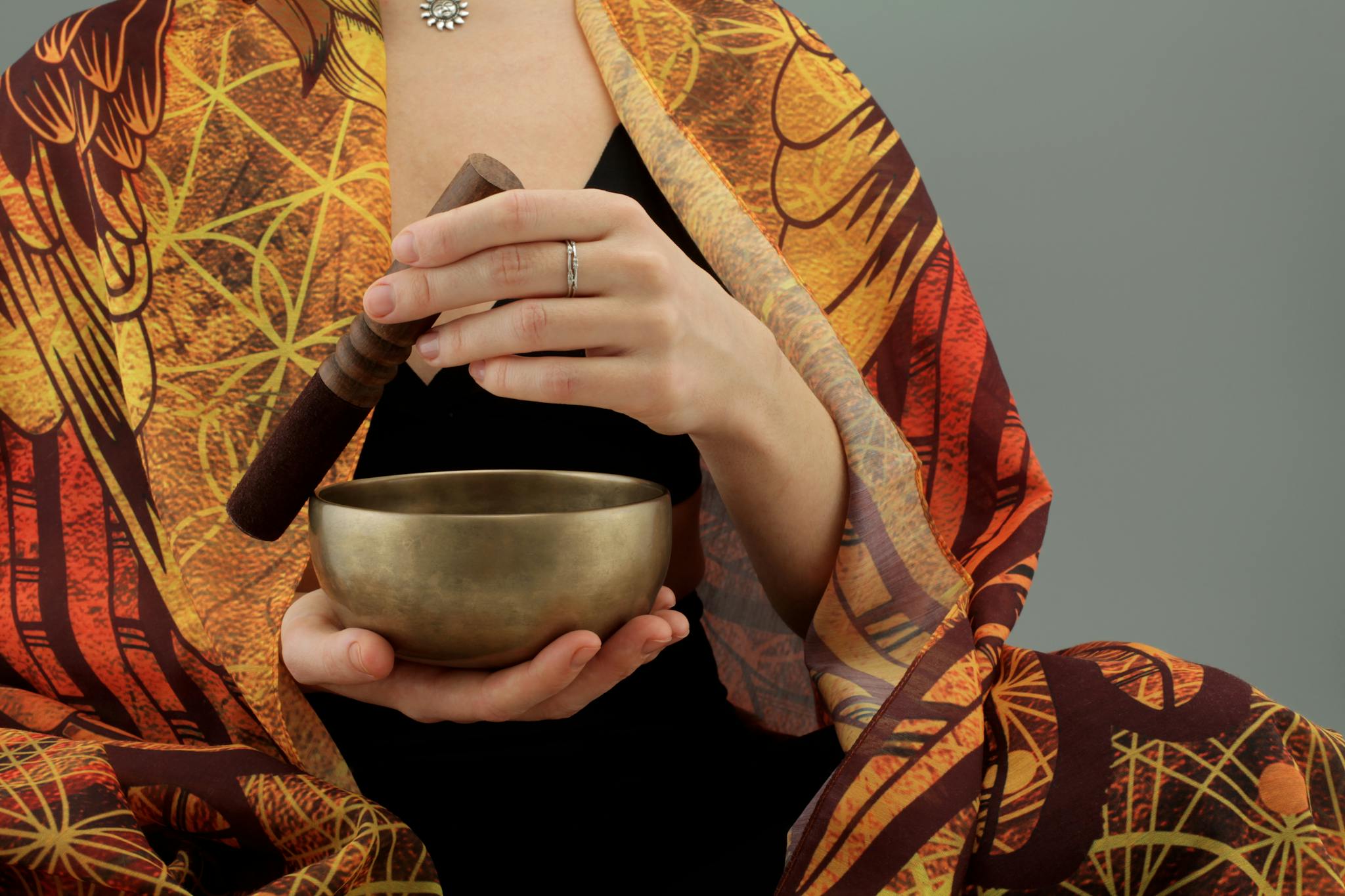 A woman with a colorful shawl holds a Tibetan singing bowl and wooden mallet, creating a serene atmosphere.